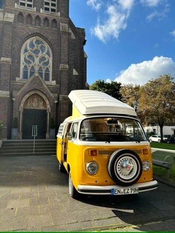 Gelber VW-Bus mit aufgestelltem Dach vor einer Kirche